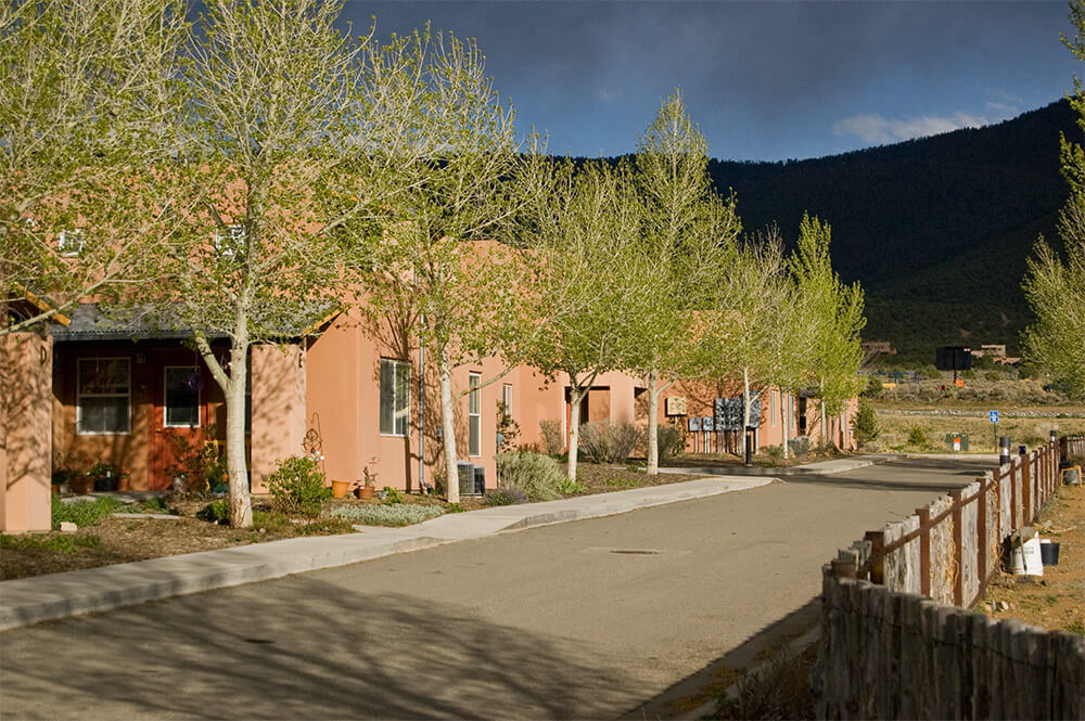 Tree-lined street of adobe-style homes at Loma Parda in Taos with the mountainside behind