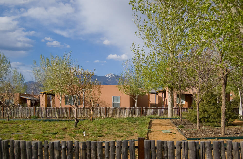 Homes at Loma Parda behind a traditional coyote fence with snow on the mountains beyond, Taos NM