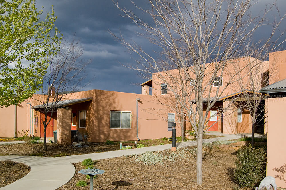 Curved courtyard walkway between one- and two-story buildings at Loma Parda under a stormy Taos sky