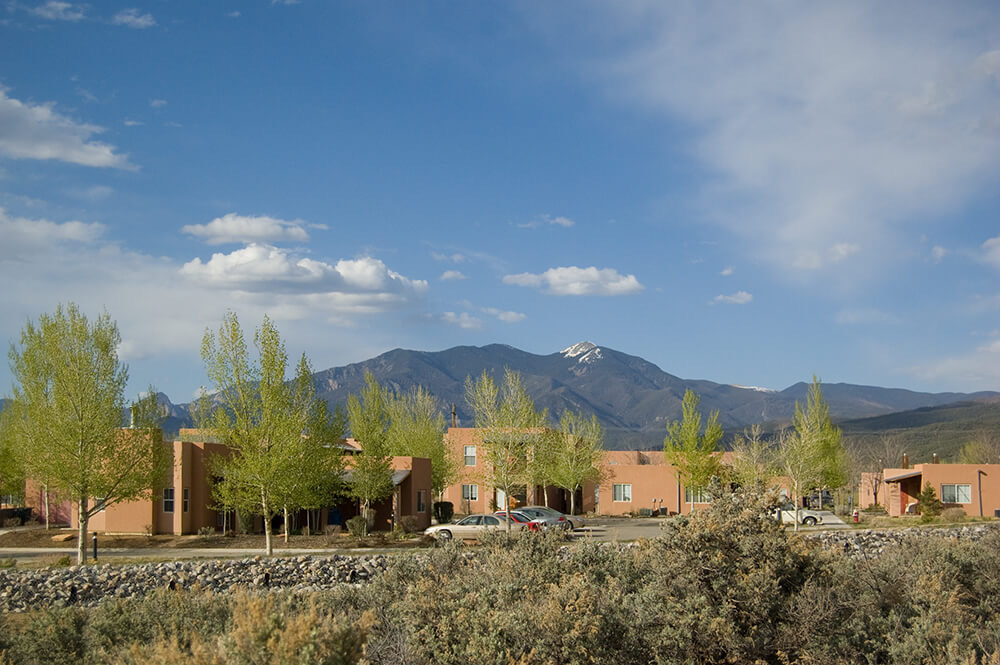 Wide view of Loma Parda in Taos, NM with snow-capped Taos Mountain rising behind the community